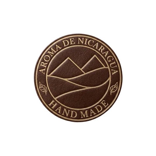 Aroma de Nicaragua-logotyp i brunt och guld med stiliserade berg, tobaksblad och texten Hand Made.